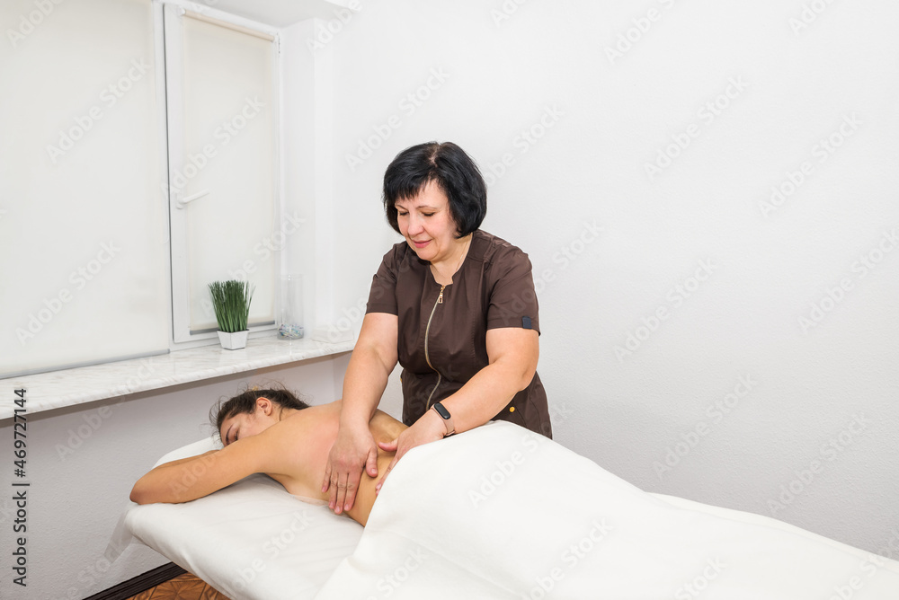 A woman massage therapist gives a back massage to a young girl A woman massage therapist gives a back massage to a young girl