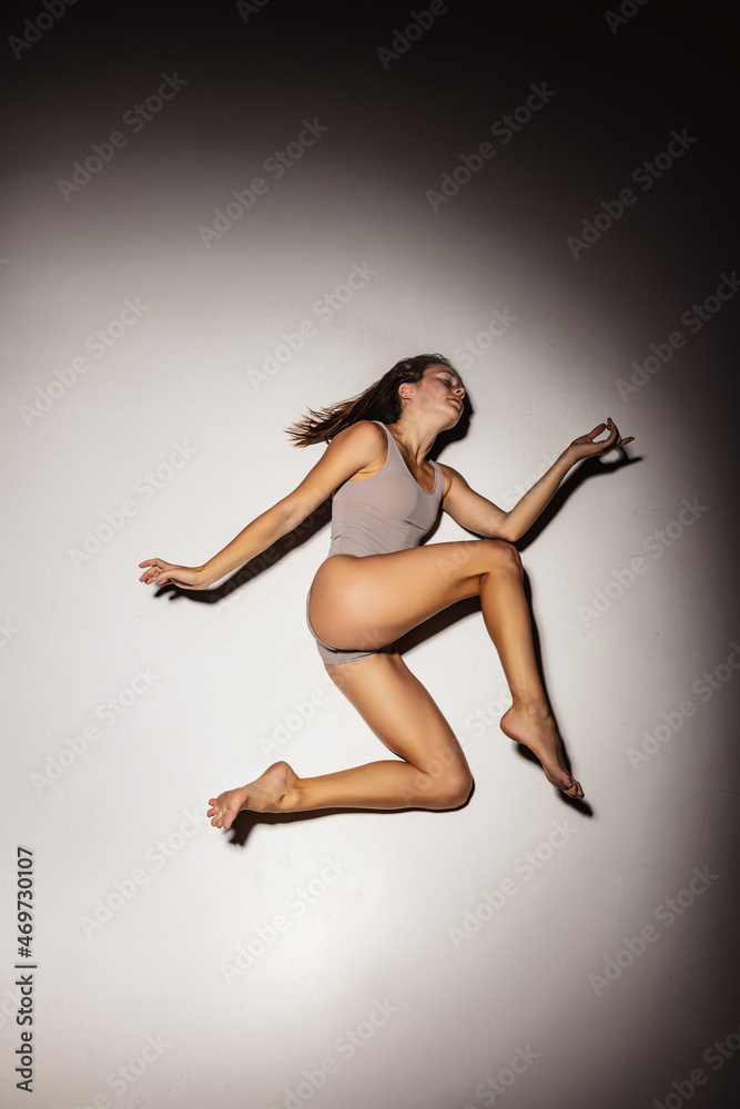High angle view of young flexible, graceful girl, female contemp dancer in art performance isolated on dark studio background in spotlight.