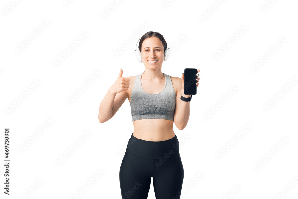 Smiling fit woman, holding mobile phone, and showing thumb up at camera over white background Smiling fit woman, holding mobile phone, and showing thumb up at camera over white background