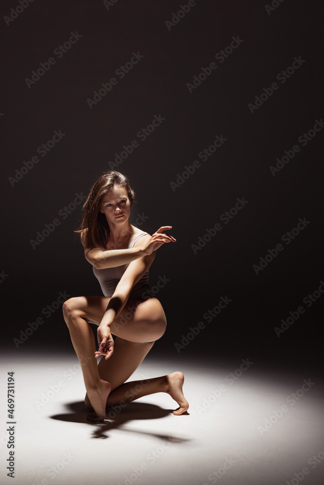 Portrait of young flexible contemp dancer dancing isolated on dark studio background in spotlight. Art, beauty, inspiration concept.