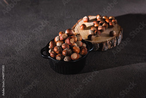 whole hazelnuts in a dark cup and on a wooden board with bark on a table on a dark textured background