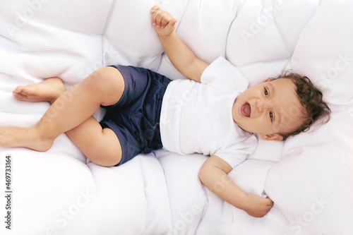 Little cheerful baby lies on a white soft mattress. Happy childhood lifestyle.