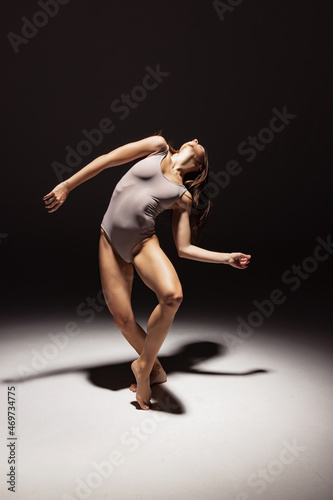 Fototapeta Naklejka Na Ścianę i Meble -  Dynamic portrait of young flexible contemp dancer dancing isolated on dark studio background in spotlight. Art, beauty, inspiration concept.