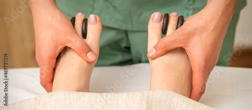 Massager doing feet and toes massage with rocks between a female toes