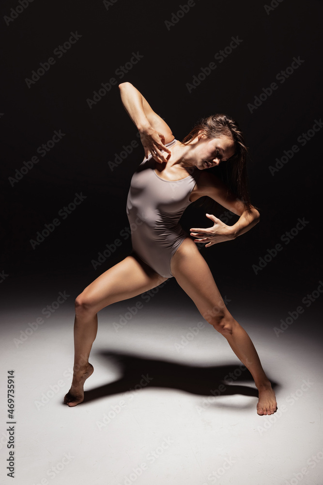 Dynamic portrait of young flexible contemp dancer dancing isolated on dark studio background in spotlight. Art, beauty, inspiration concept. Dynamic portrait of young flexible contemp dancer dancing isolated on dark studio background in spotlight. Art, beauty, inspiration concept.