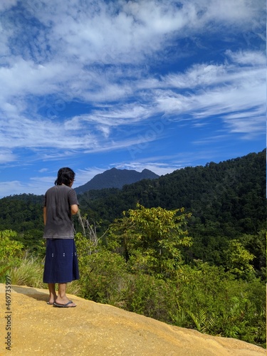 a young man wearing a sarong is enjoying the beauty of nature from the top of the hill photo