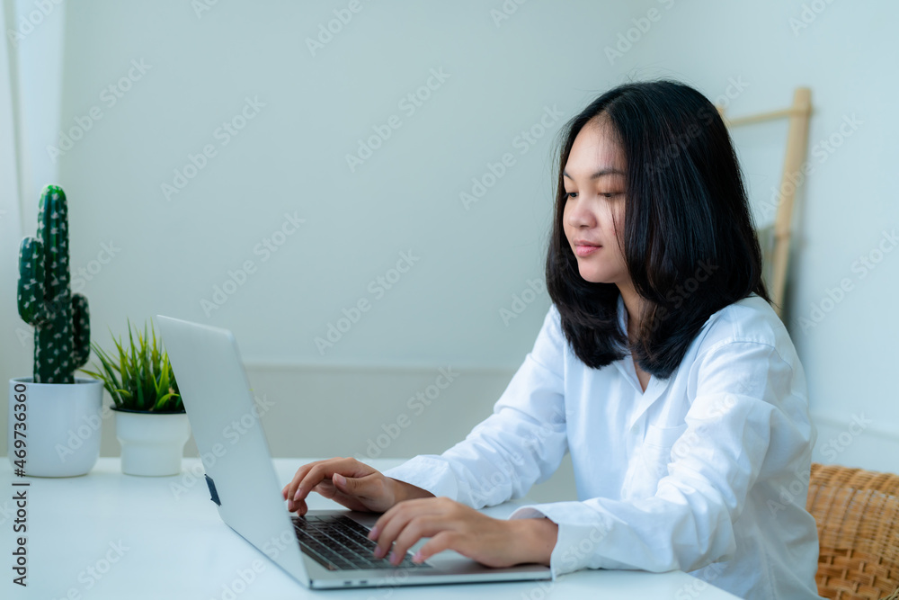 Portrait Cute Asian teen with long hair Wearing a white shirt, sitting online studying with a laptop on the bedroom table with a thoughtful face. Portrait Cute Asian teen with long hair Wearing a white shirt, sitting online studying with a laptop on the bedroom table with a thoughtful face.