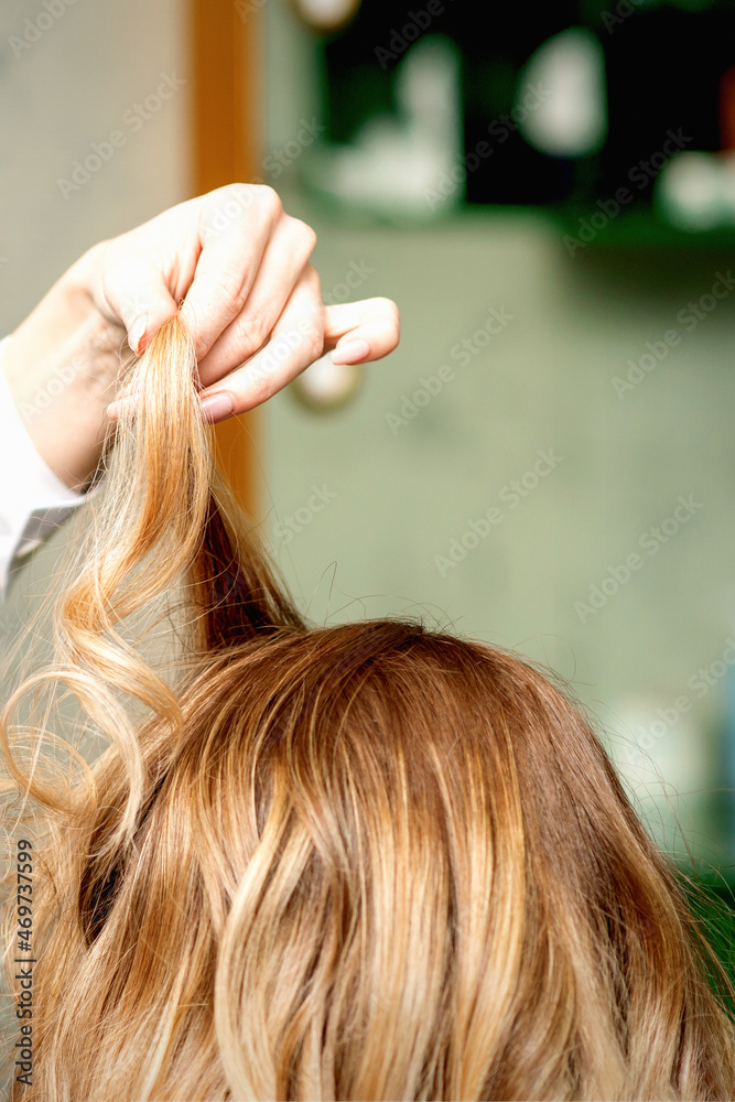 Fototapeta premium Female coiffeur fixing hairstyling of blonde woman with hairspray in a beauty salon