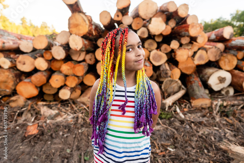 Girl in front of pile of logs glances at camera photo