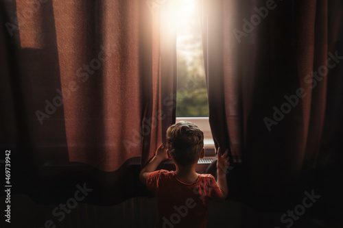 Back view of boy peaking outside through windows photo