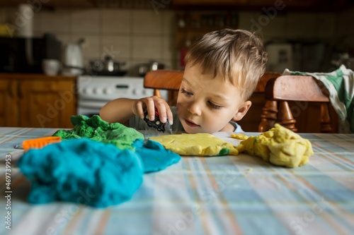 Blonde boy playing on kitchen table with colorful play doh and c photo