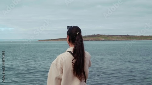 A young tourist girl on the beach by the sea with a phone in her hand will take pictures of the landscape around her.