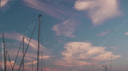Oscillating yacht masts against the blue sky with clouds.