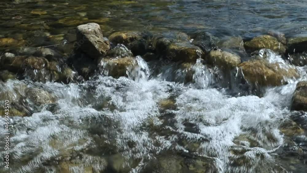 A stream of water with foam and a rocky bottom of a mountain river. A stream of water with foam and a rocky bottom of a mountain river.