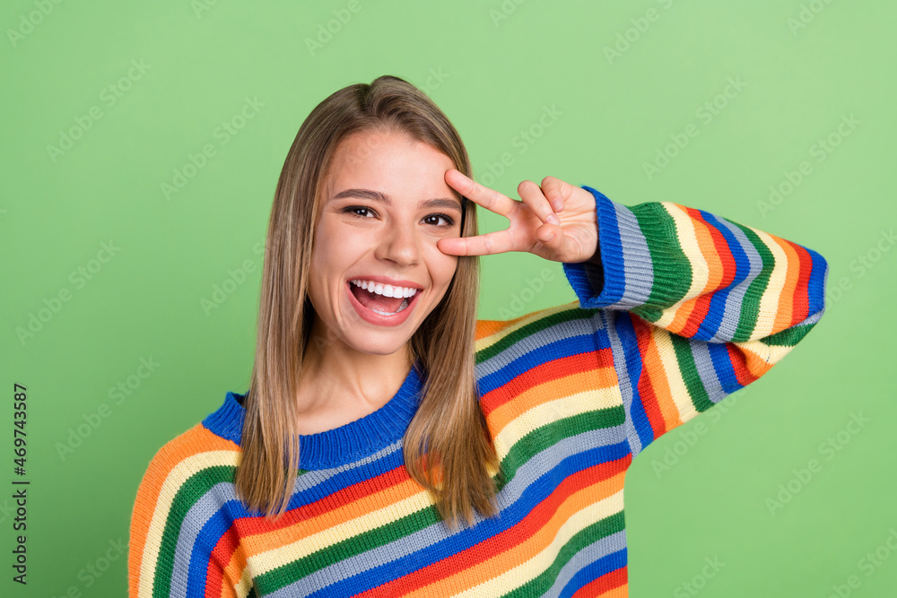 Photo portrait smiling girl showing v-sign gesture wearing pullover laughing isolated pastel green color background Photo portrait smiling girl showing v-sign gesture wearing pullover laughing isolated pastel green color background