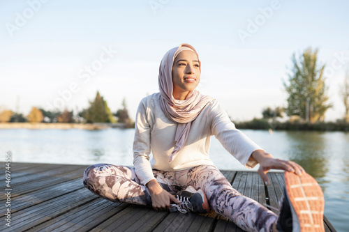 Positive Arab woman doing stretching exercise on embankment photo