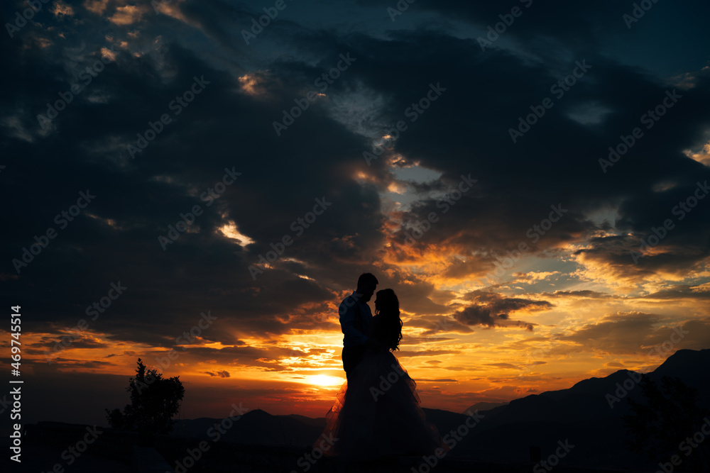 Silhouettes of the bride and groom who are embracing on Mount Lovcen overlooking the Bay of Kotor at sunset 