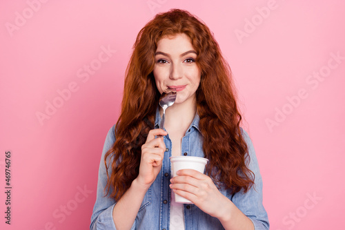 Photo of sweet hungry young woman wear denim shirt ready eat yogurt licking spoon smiling isolated pink color background