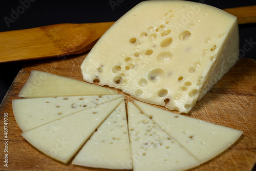 Yellow cheese on a black background. Slice of cheese with holes on a wooden board on a dark background