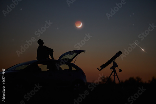 Silhouette of a man, telescope and countryside under the starry skies.