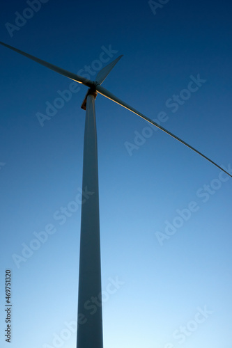 Close up, side view of a wind tower turbine electricity gererator, renewable energy source. Wind Farm with blue sky and without clouds © OneWellStudio