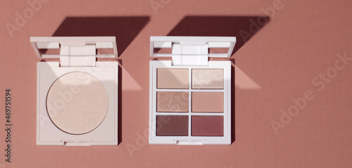 Eye shadow palette and highlighting powder on pink clean background. Cosmetic product background