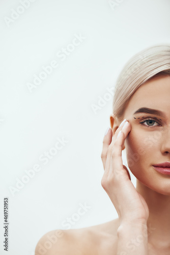 Plastic Surgery Operation. Cropped photo of pretty and young blonde woman touching her face with black surgical lines on eyelids and looking at camera photo