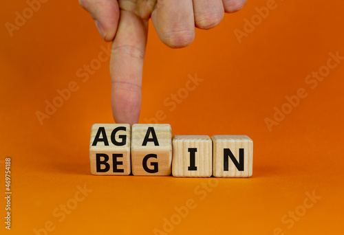 Begin again symbol. Businessman turns wooden cubes and changes the word begin to again. Beautiful orange table, orange background. Business and begin again concept. Copy space.