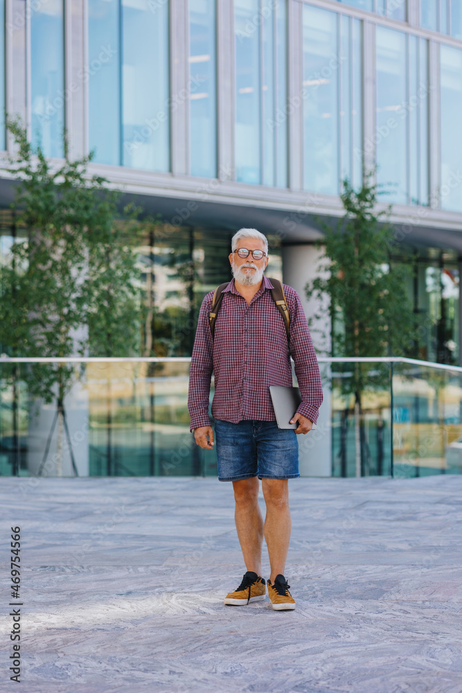 Naklejka premium an adult gray-haired man with a beard goes to the office to work. a senior businessman in a shirt and with a laptop is making a career in a large company. a stylish European talks on the phone with