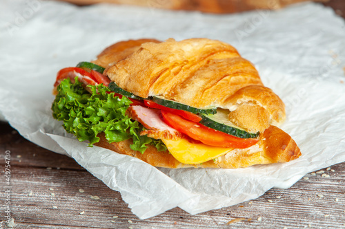 Breakfast of Fresh croissant with ham, cheese and salad leaf on white wooden background.