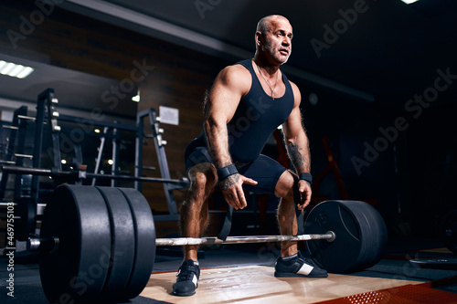 Older sportsman preparing to exercise deadlift with barbell while on cross training in a gym.