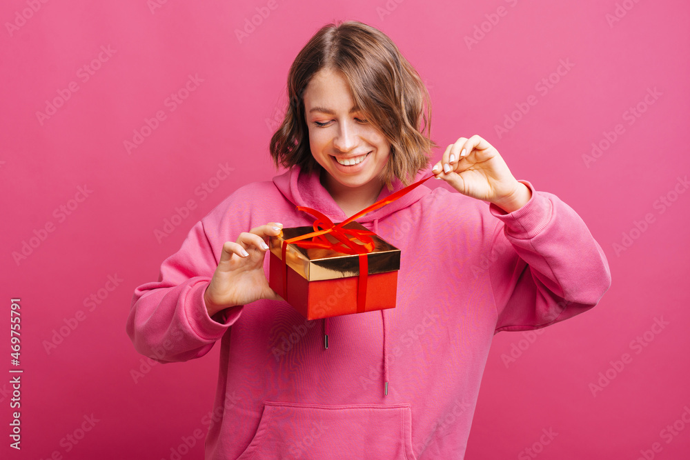 Happy young woman standing over pink background and opening red gift box, excited girl. Happy young woman standing over pink background and opening red gift box, excited girl.