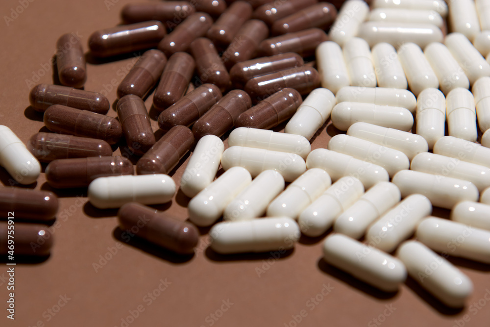 Many white and brown capsule pills on a colorful background. Health supplements and medicines Many white and brown capsule pills on a colorful background. Health supplements and medicines
