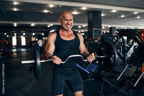 Muscular older man working out in gym doing exercises with barbell at biceps. Bodybuilding concept