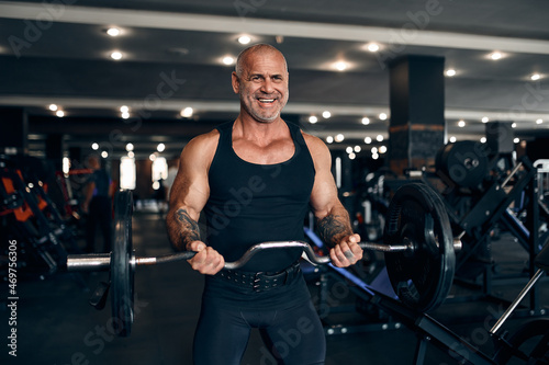 Muscular bald man working out in gym doing exercises with barbell at biceps. Bodybuilding concept
