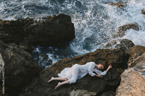 woman in long white dress wet hair lying on a rocky cliff landscape