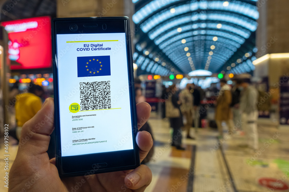 Woman showing on smartphone EU Digital Covid Certificate with quad code. Train station background.