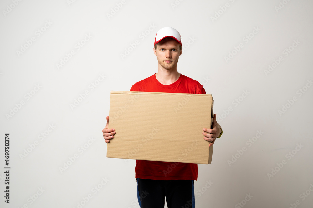 Male employee in in red uniform working as courier dealer and holds cardboard box isolated on white background, studio portrait. Service concept. Mock up copy space.