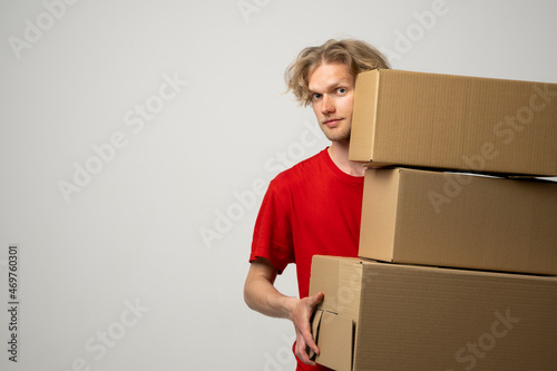 Courier in a red uniform holding a stack of cardboard boxes. Delivery man delivering postal packages over white studio background.
