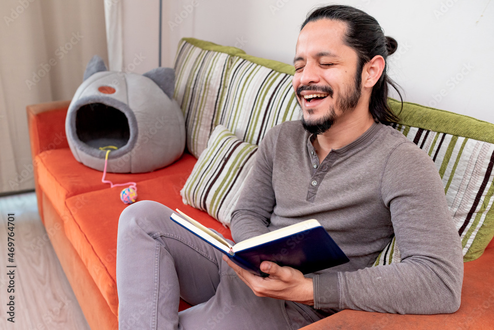 Young man reading a book at home sitting on the couch in the living room Young man reading a book at home sitting on the couch in the living room
