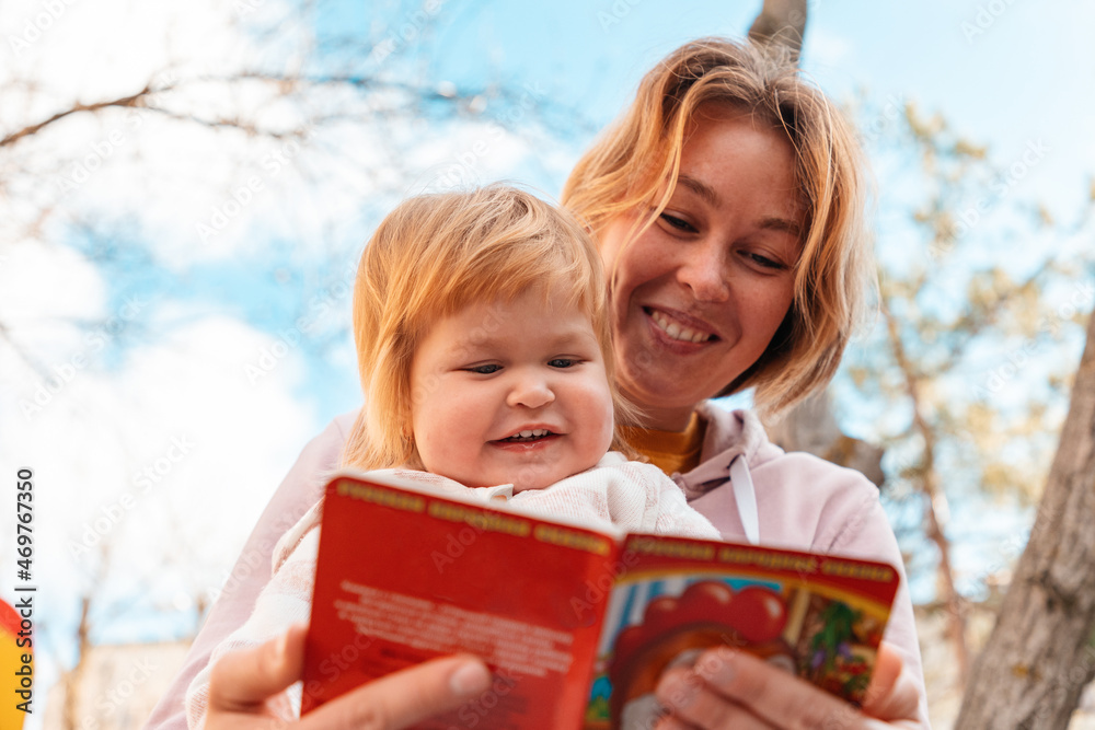 Happy young mother reads a book to her little daughter while relaxing in the park. Bottom view. The concept of upbringing and preschool education of children Happy young mother reads a book to her little daughter while relaxing in the park. Bottom view. The concept of upbringing and preschool education of children