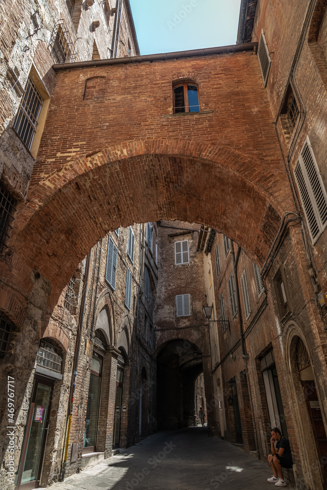 Narrow Street in Historic Center of Siena, Tuscany, Italy. Old brick and stucco houses, arches and cobblestone pavement