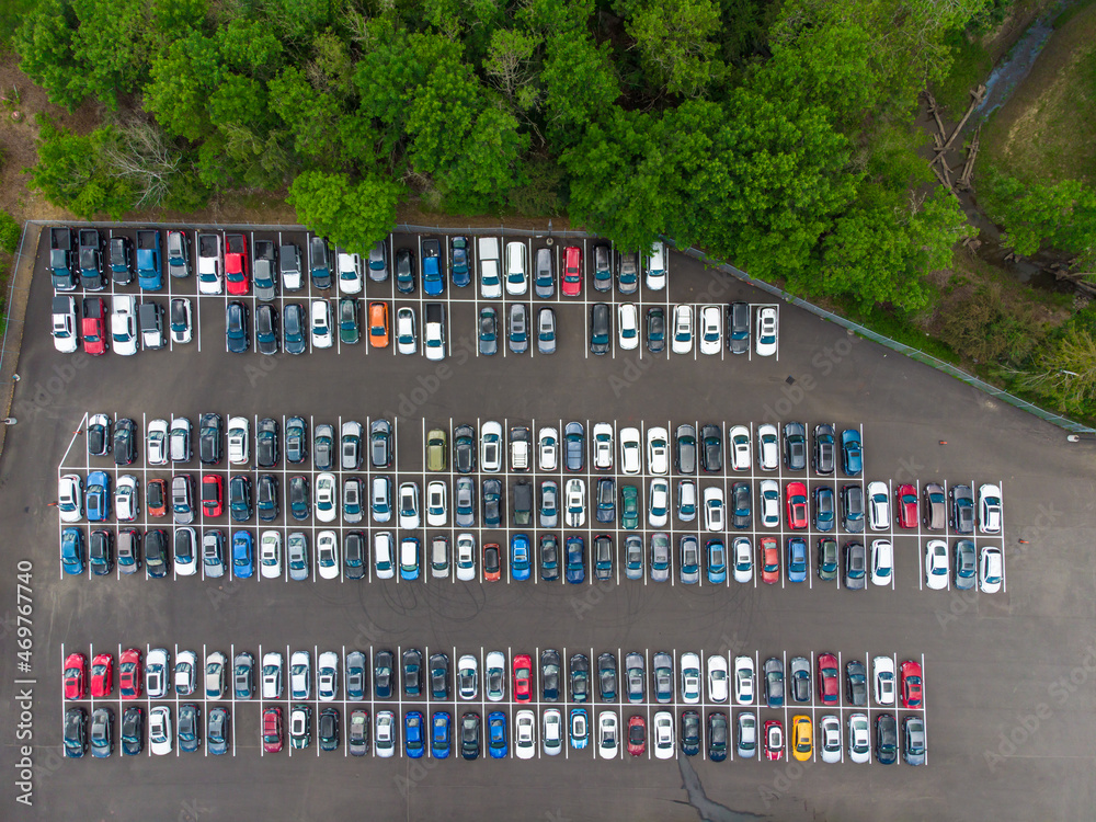 Shooting from a drone. Large car parking. There are many green trees around, many parked cars. Travel, tourism, recreation, map, topography, infrastructure, environmental and social issues.