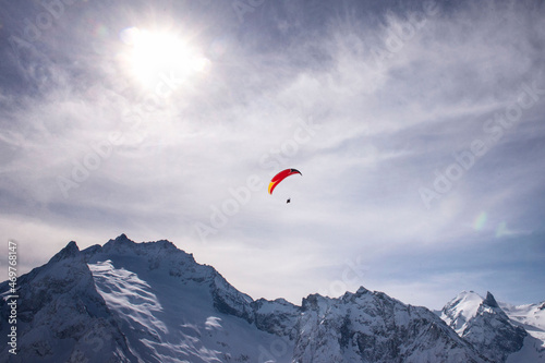 Bright red paraglider on a winter cloudy day flies over the snow-capped mountains of the Caucasus Range