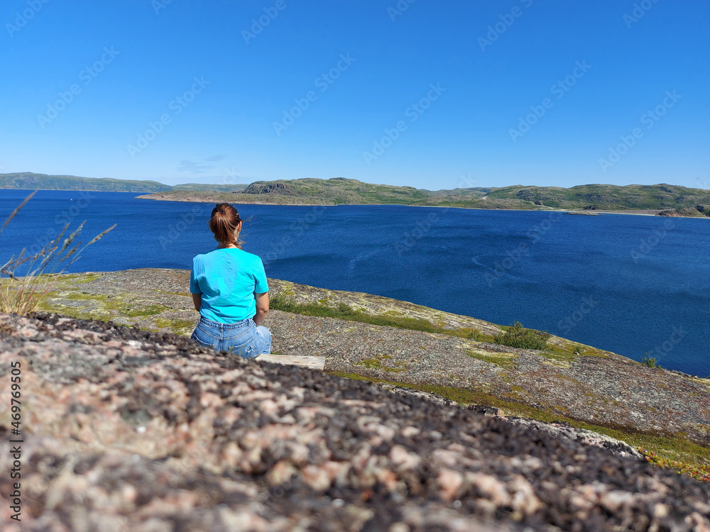 A girl sits on a stony deserted shore looks into the distance and enjoys loneliness. State of mind concept.
