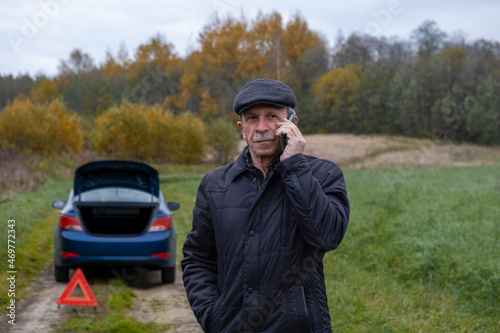 Adult pensioner calls technical assistance on smartphone after his faulty car outside city. Selective focus.