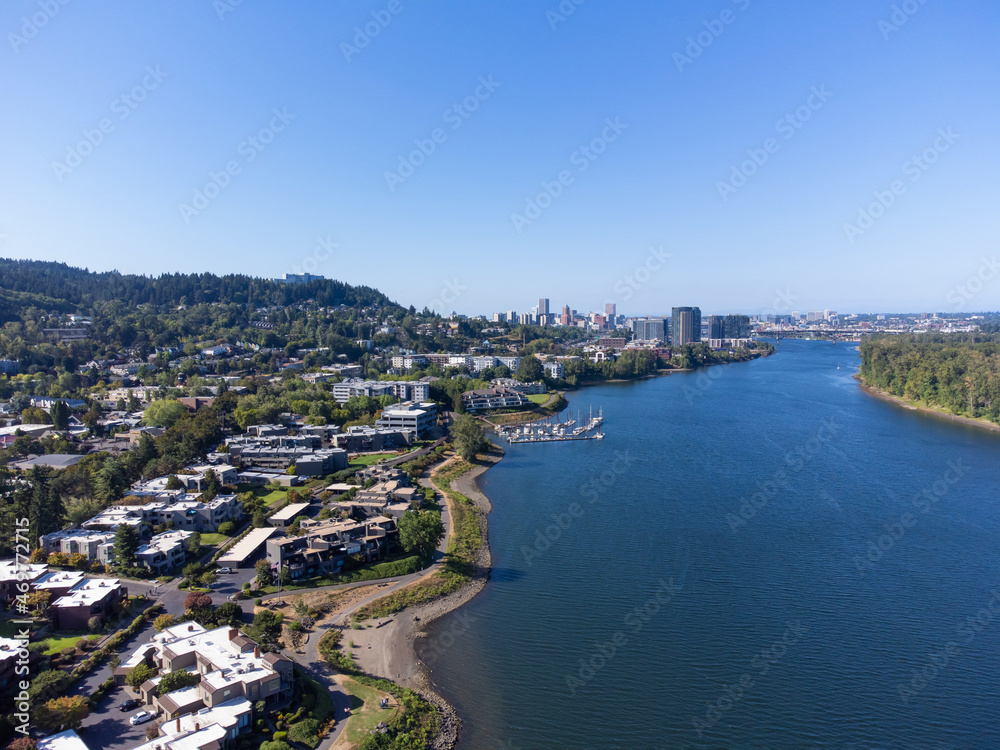 Aerial view. A small green city on the banks of a large blue river. Mountains can be seen in the distance. Blue cloudless sky. Beautiful landscape. Ecology, tourism, housing.