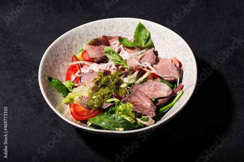 salad with roast beef and oyster mushrooms, herbs, cherry, basil and pesto sauce, black background, hard light
