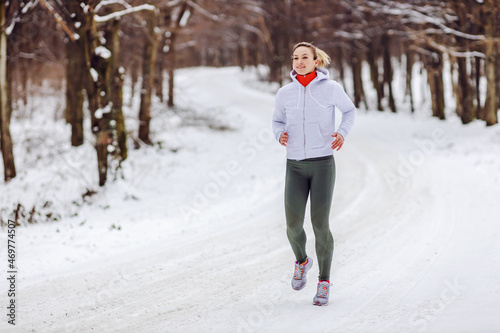 Fit sportswoman running in nature on a snowy winter day. Cold weather, snow, healthy life, fitness, healthy habits