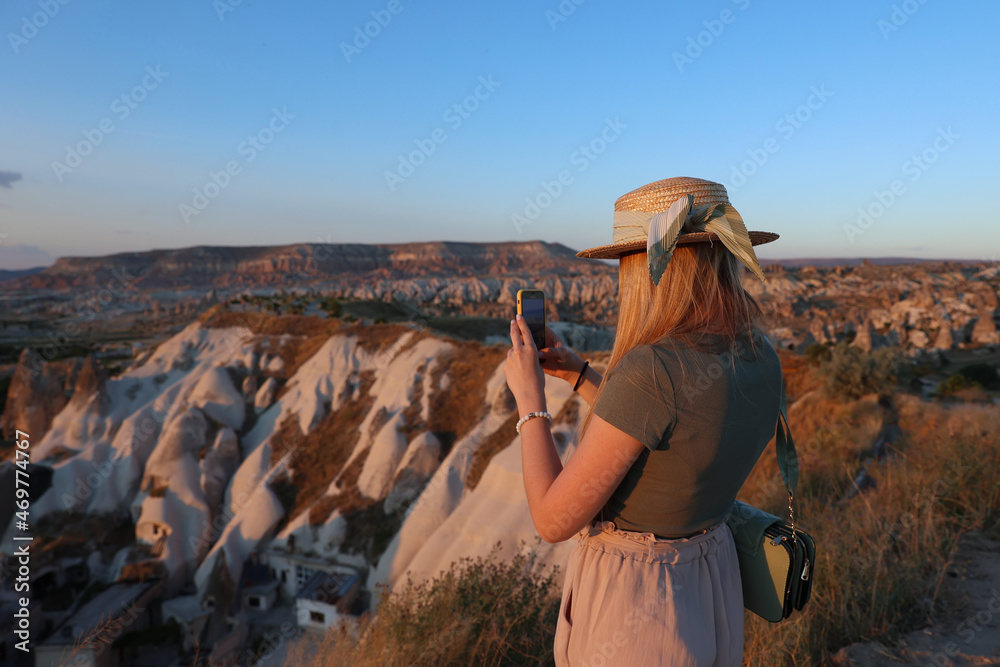 Woman taking photo of beautiful landscape in Cappadocia with mobile camera, dreamy travel concept